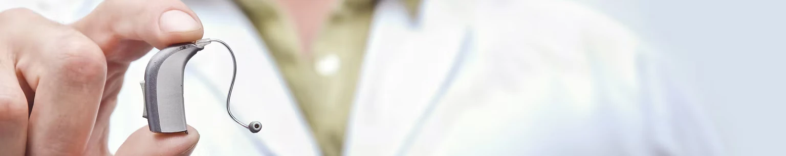 Ein Hörgeräteakustiker hält ein modernes, kleines Hörgerät vor weißem Hintergrund.